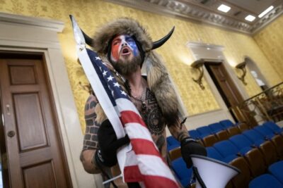 WASHINGTON, DC - JANUARY 06: Jacob Chansley, also known as the "QAnon Shaman," screams "Freedom" inside the U.S. Senate chamber after the U.S. Capitol was breached by a mob during a joint session of Congress on January 6, 2021 in Washington, DC. Congress held a joint session to ratify President-elect Joe Biden's 306-232 Electoral College win over President Donald Trump. Pro-Trump protesters illegally entered the U.S. Capitol building following rallies in the nation's capital. WIN MCNAMEE/GETTY IMAGES